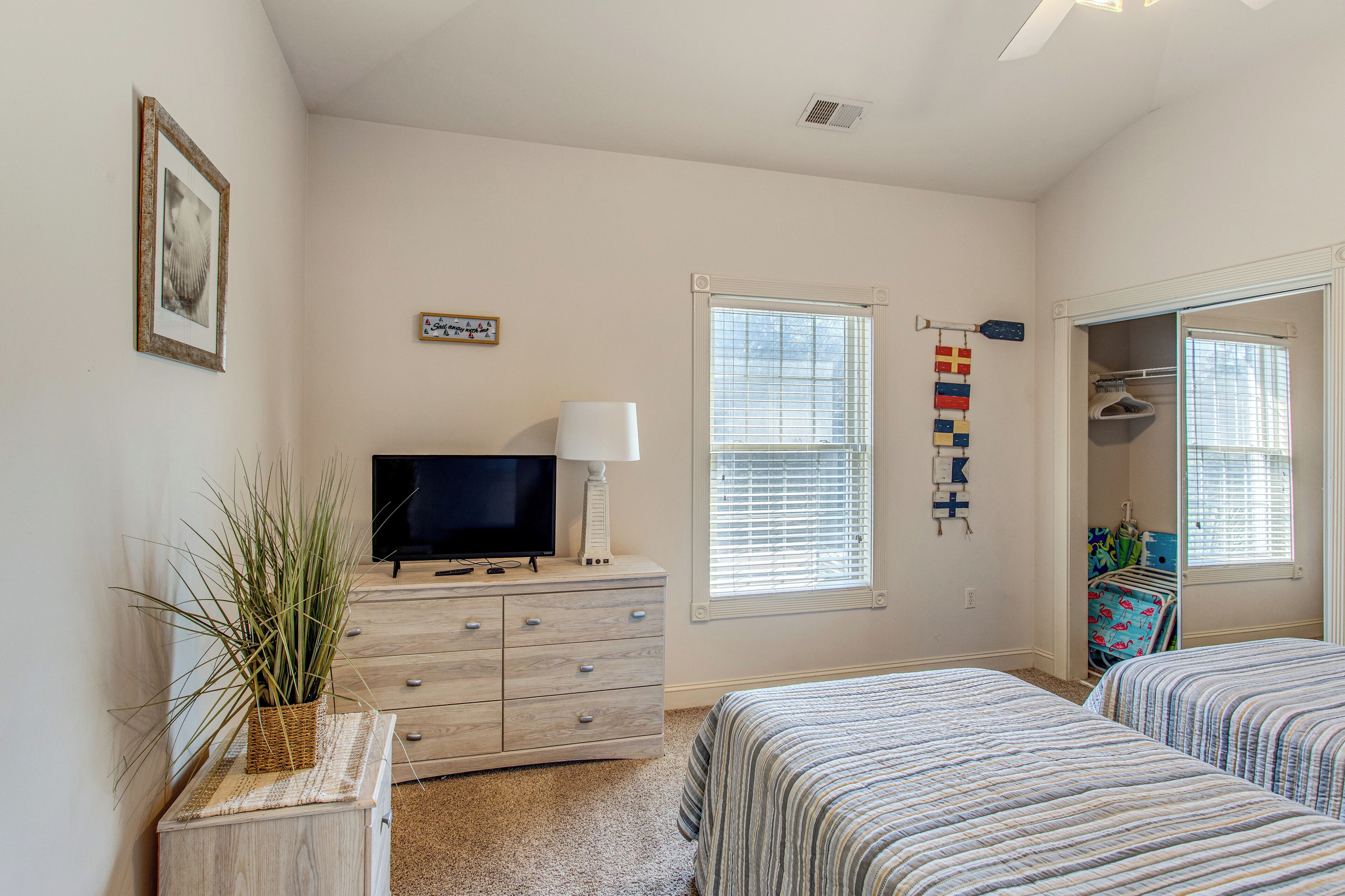A bedroom with two beds, a TV on a dresser, a window with blinds, and a closet with hanging clothes.