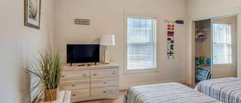 A bedroom with two beds, a TV on a dresser, a window with blinds, and a closet with hanging clothes.