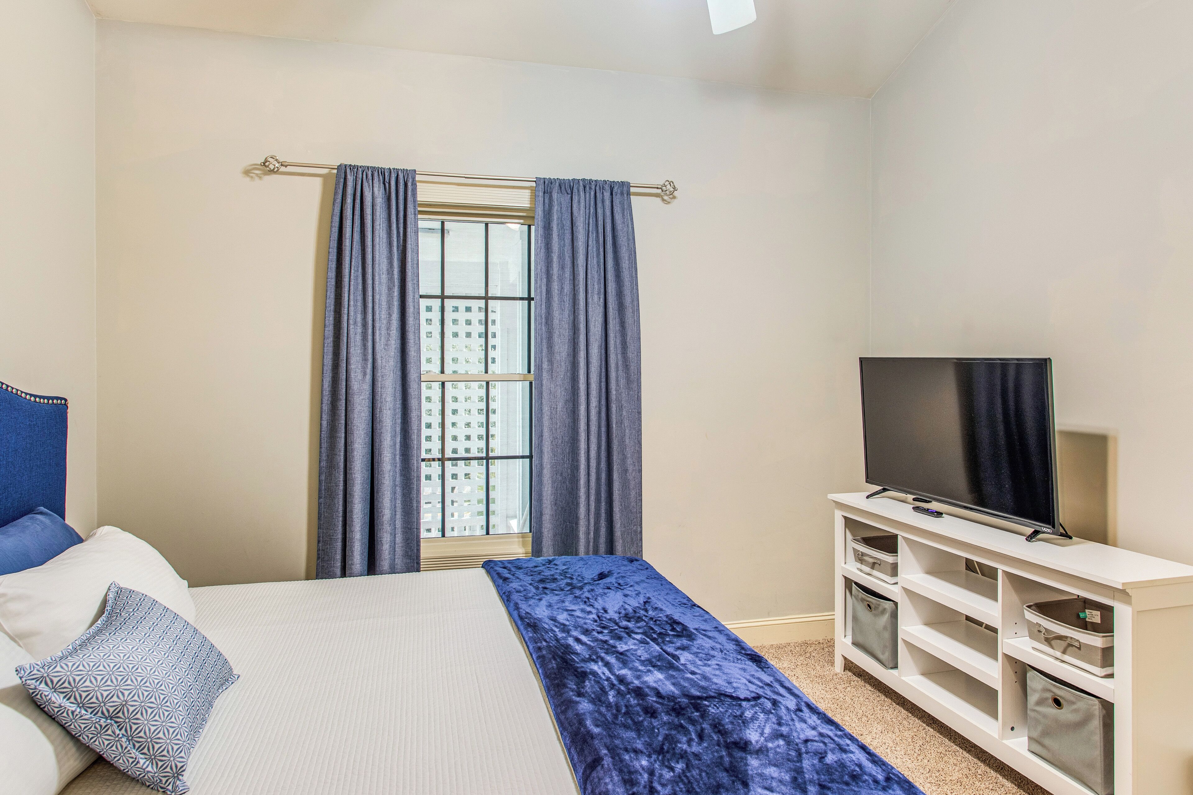 A bedroom with a bed, a TV, and a window with curtains.