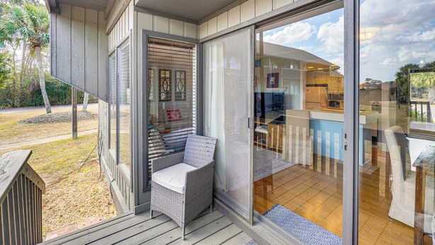 A covered outdoor area with a wicker chair and a glass door leading to a kitchen area. - Golfer's Getaway! Modern Diamondhead Condo (Diamondhead)