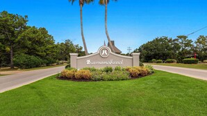 A sign with the name 'Diamondhead' surrounded by well-maintained grass and palm trees. - Golfer's Getaway! Modern Diamondhead Condo (Diamondhead)