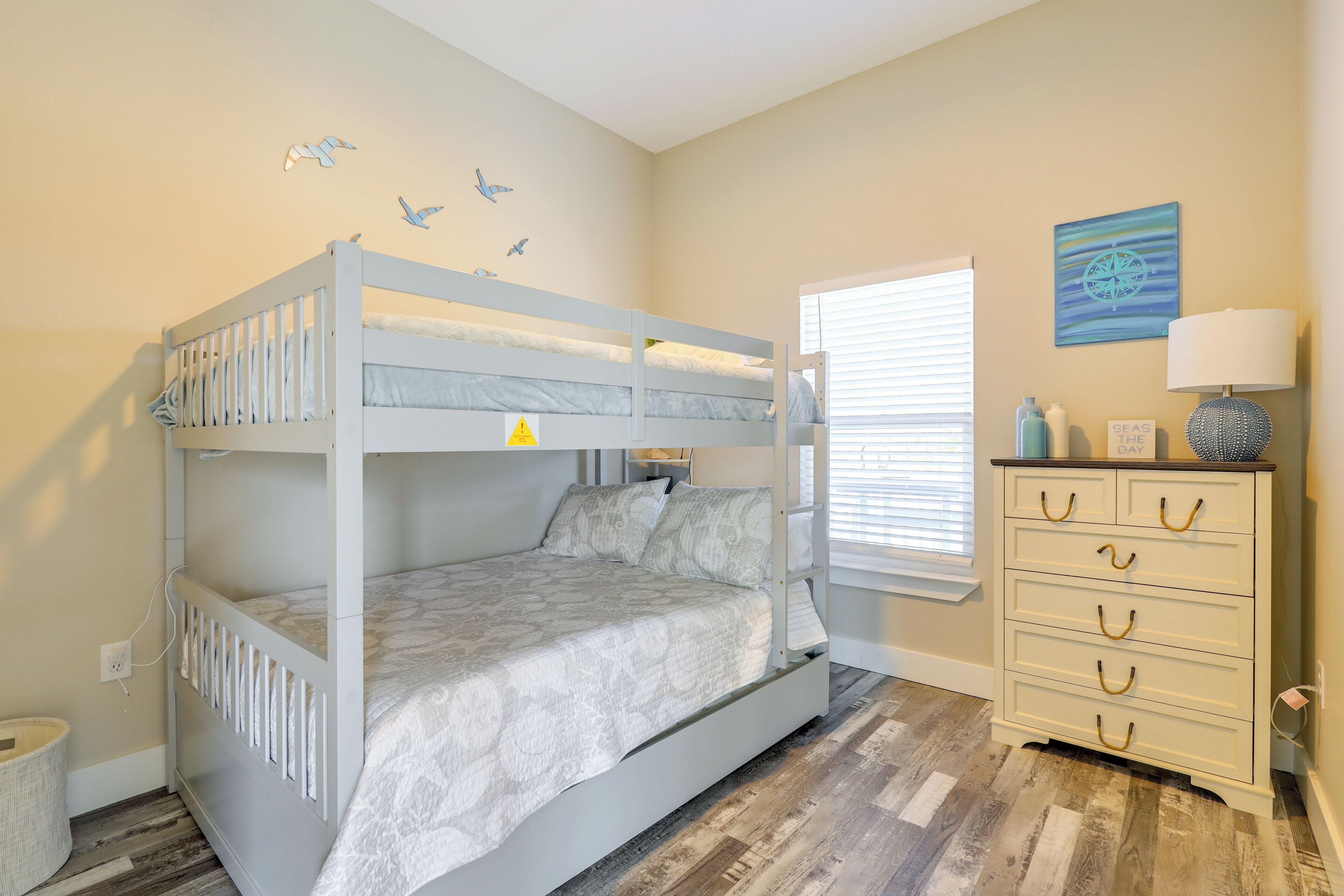 A bunk bed with a patterned bedspread, a dresser with drawers, a lamp, and a wall clock.