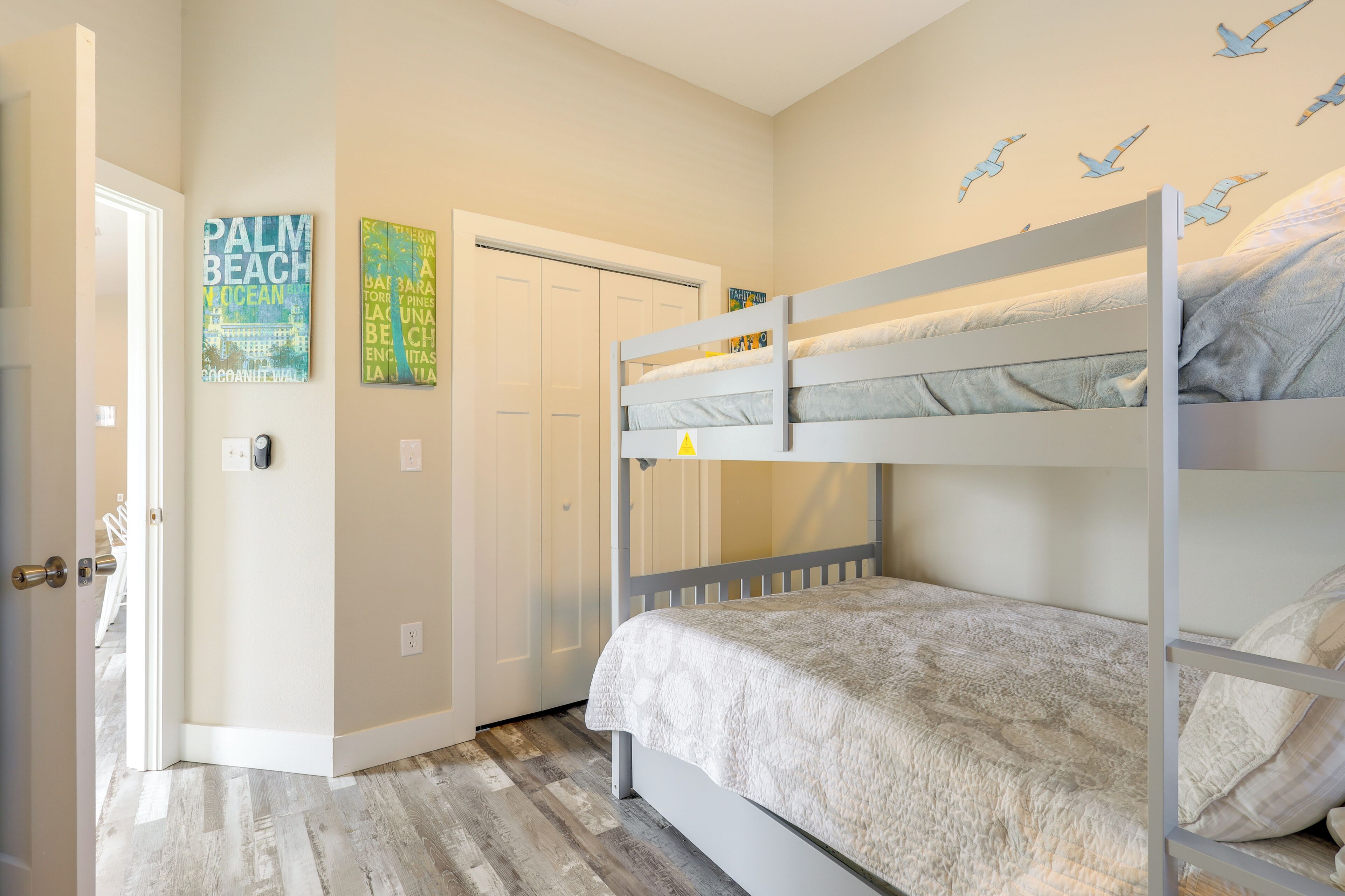 A bunk bed room with a door, wall art, and a wooden floor.