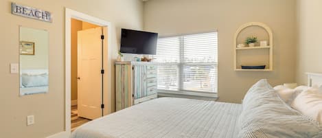 A bedroom with a bed, a television, a window with blinds, a dresser, and a wall-mounted shelf.