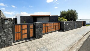 Una casa moderna con un muro in pietra, un cancello in legno e un vialetto lastricato.