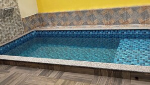 A swimming pool with blue mosaic tiles, surrounded by wooden decking and a yellow wall. - House with pool in Itanhaém | Ideal for families and groups (Itanhaém)