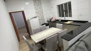 A modern kitchen with white tiles, a dining area with a table and chairs, and a grey sofa. - House with pool in Itanhaém | Ideal for families and groups (Itanhaém)