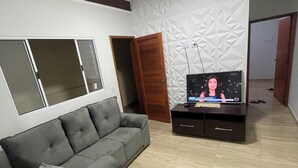 A modern living room with a grey sectional sofa, a TV on a wooden stand, and a patterned wall. - House with pool in Itanhaém | Ideal for families and groups (Itanhaém)