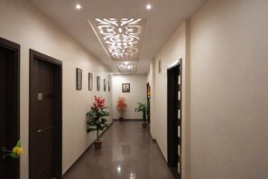 A hallway with framed pictures on the walls, potted plants, and a decorative ceiling light fixture. - Hotel RK Palace (Gandhinagar)
