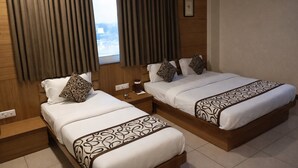 A hotel room with two beds, each with patterned bedspreads, a bedside table with a coffee maker, and a window with curtains. - Hotel RK Palace (Gandhinagar)