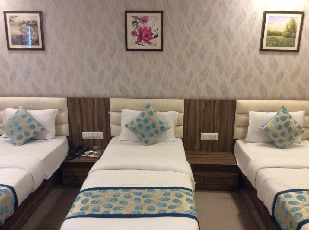 A hotel room with three beds, each with a white headboard and blue patterned pillows. There are framed pictures on the wall above the beds.