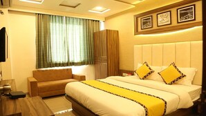 A hotel room with a bed, a sofa, a TV, and a wardrobe. - Hotel RK Palace (Gandhinagar)