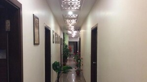 A hallway with framed pictures on the walls, potted plants, and a shiny floor. - Hotel RK Palace (Gandhinagar)