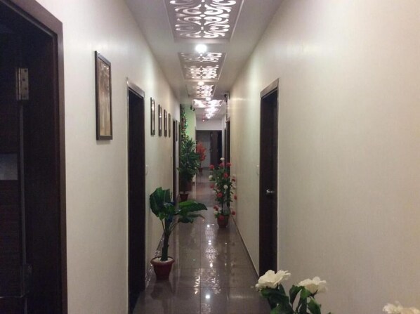 A hallway with framed pictures on the walls, potted plants, and a shiny floor. - Hotel RK Palace (Gandhinagar)