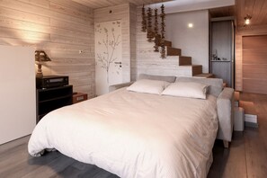 A bedroom with a large bed, a nightstand, a dresser, and a staircase leading to another room.