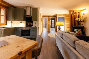 A modern kitchen with grey cabinets, a wooden dining table, and a sofa in the living area. - Hirondelle Chalet (Sainte-Foy-Tarentaise)