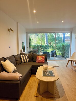 Un salon moderne avec un canapé d’angle, une table basse ronde et une vue sur une terrasse extérieure, accessible par de grandes portes-fenêtres coulissantes.