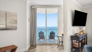 A hotel room with a balcony, a flat-screen TV, a small table, and two Adirondack chairs. - TW 1600-King Bed-Arcade-Sauna-New Listing (Panama City Beach)