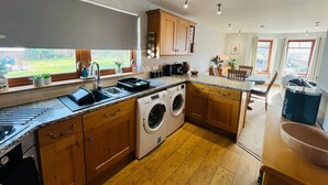 A modern kitchen with a built-in washer and dryer, wooden cabinets, and a large window providing a view of the outdoors.
