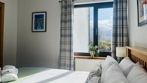 A hotel room with a bed, a window with curtains, a radiator, and a framed picture on the wall.