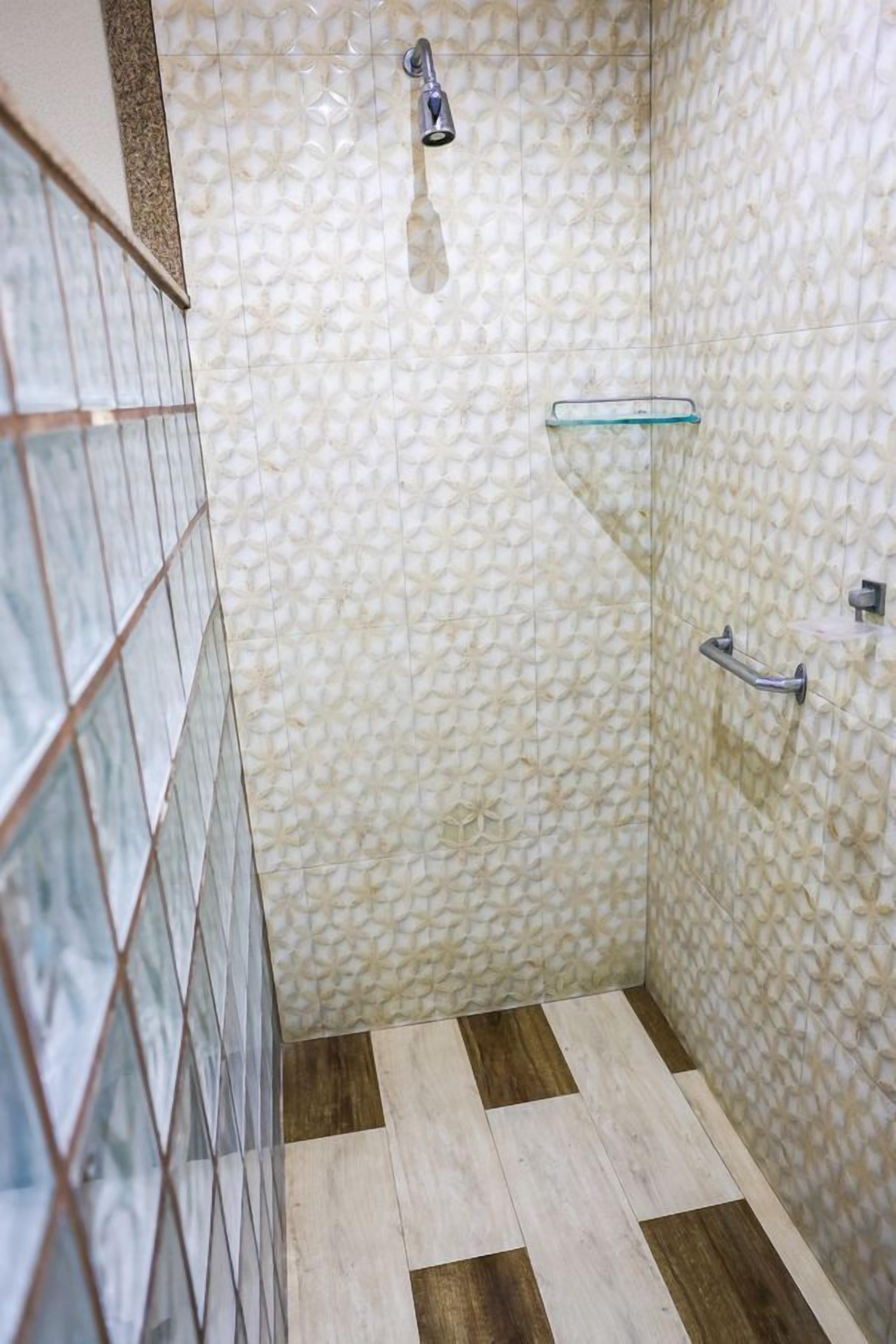 A bathroom with patterned tiles, a shower, a glass shelf, and a handrail.