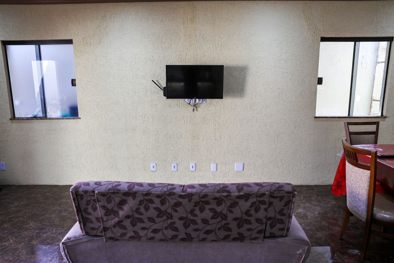 A room with a sofa, a TV mounted on the wall, and two windows.