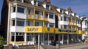 A multi-story building with 'SAVOY' and 'HOTEL' signage, featuring balconies and a reception area.
