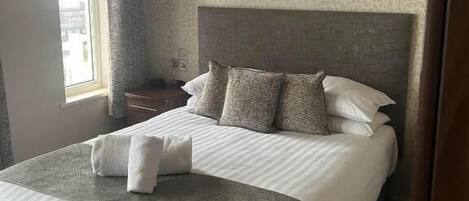 A neatly made bed with a grey and white duvet, a headboard, and a bedside table with a lamp.