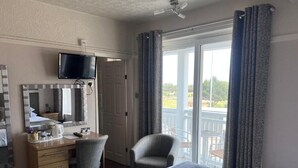A hotel room with a bed, a desk with a chair, a television, and a balcony with curtains.