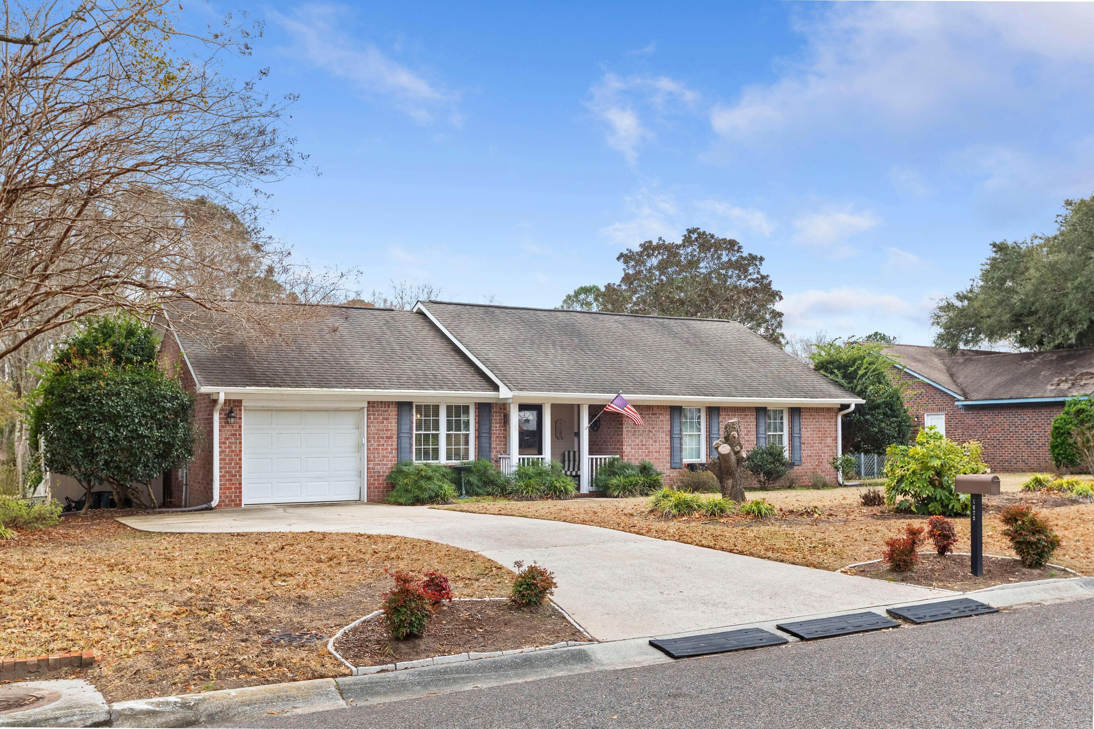 A single-story brick house with a white garage door, a front porch, and a small front yard with a flag.