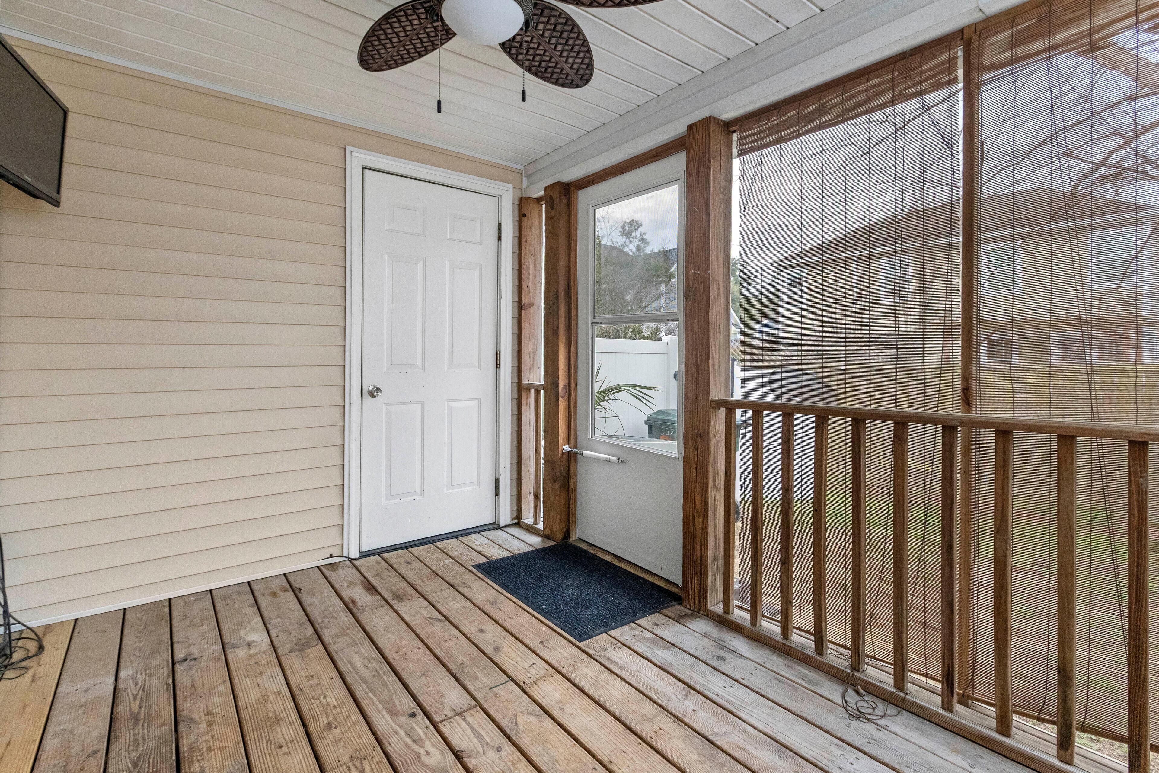 Un porche abrité avec une terrasse en bois, une porte blanche et une moustiquaire.