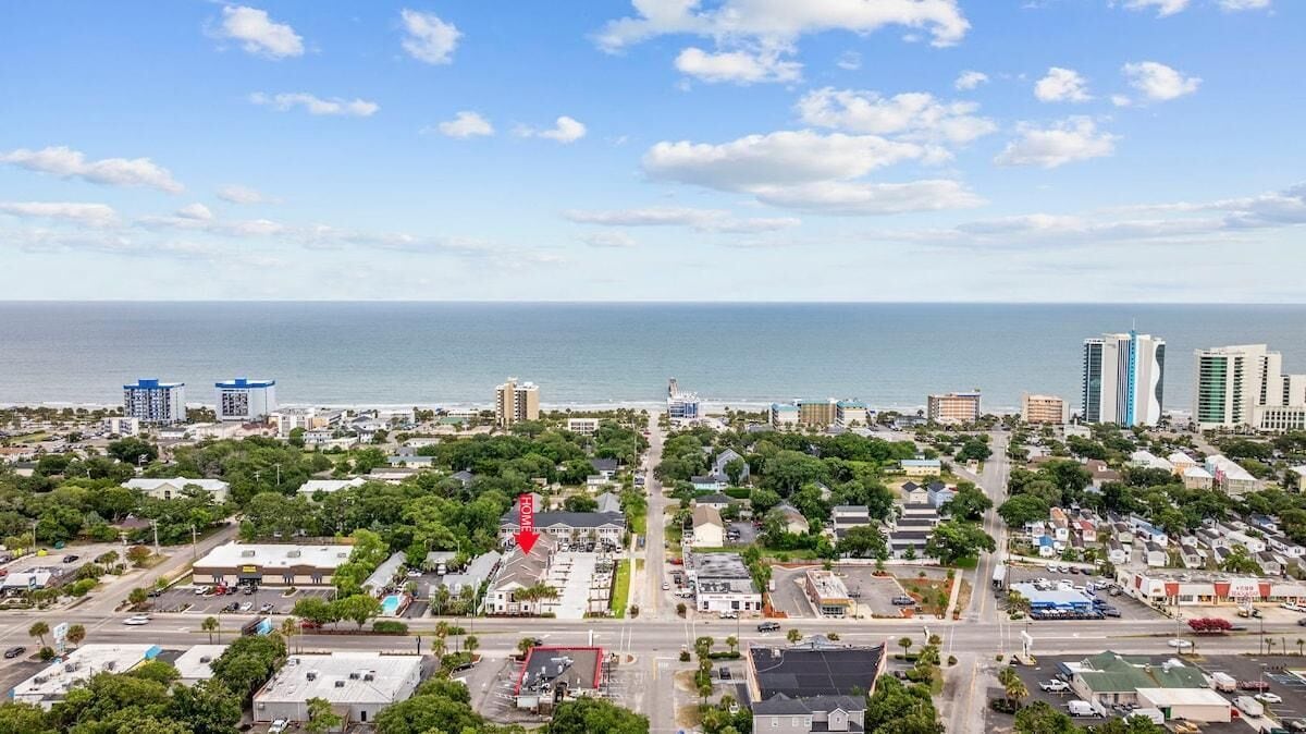 A coastal cityscape with a mix of residential and commercial buildings, a clear sky, and a view of the ocean.