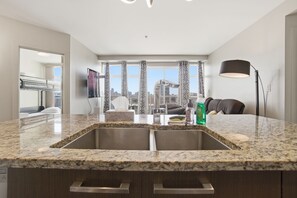 A modern kitchen with granite countertops, a double sink, and a view of the city through large windows.