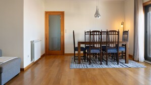 A dining area with a wooden table and chairs, a radiator, a grey sofa, and a door leading to another room.