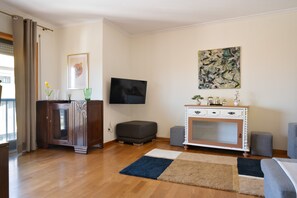 Un salon avec un plancher en bois, un téléviseur à écran plat, un meuble, un canapé et un tapis.