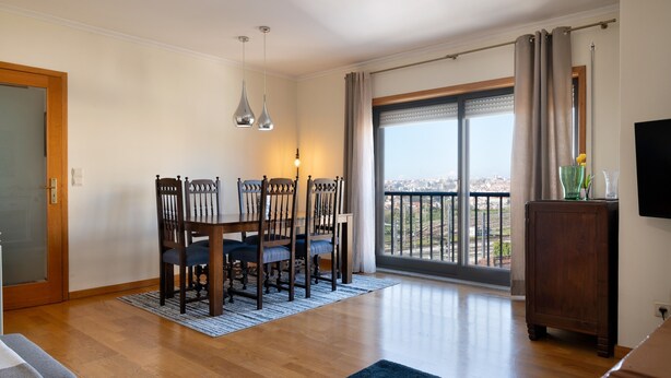 A dining area with a table and chairs, a view through a large window, and a wooden cabinet.