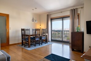 Ein Essbereich mit Tisch und Stühlen, ein Blick durch ein großes Fenster und eine Holzkommode.