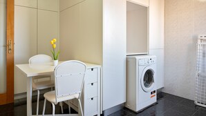 A compact room with a washing machine, a small table with a chair, and a potted plant.