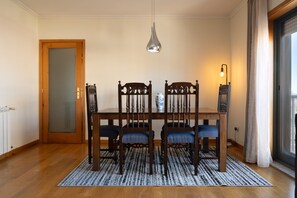 Zona pranzo con tavolo in legno, quattro sedie, lampadario, vaso e finestra con tende.