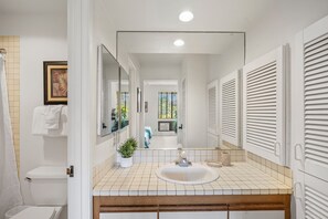 A bathroom with a white sink, mirror, and toilet. There is a potted plant on the counter and a towel hanging on the wall. - Peaceful Golf Course Retreat with Partial Ocean Views-Wailea Grand Champions #78 (Wailea, Maui)