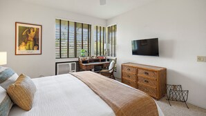 Ein Schlafzimmer mit einem Bett, einem Schreibtisch, einer Kommode, einem Fernseher und einem Deckenventilator.