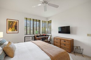 A bedroom with a bed, a desk, a dresser, a television, and a ceiling fan. - Peaceful Golf Course Retreat with Partial Ocean Views-Wailea Grand Champions #78 (Wailea, Maui)