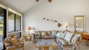 Ein Wohnzimmer mit einem Ecksofa, einem Glastisch und einem Deckenventilator.
