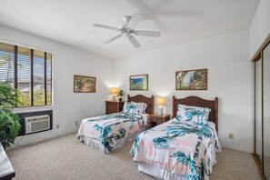Une chambre avec deux lits, un ventilateur de plafond et des œuvres d’art accrochées aux murs.