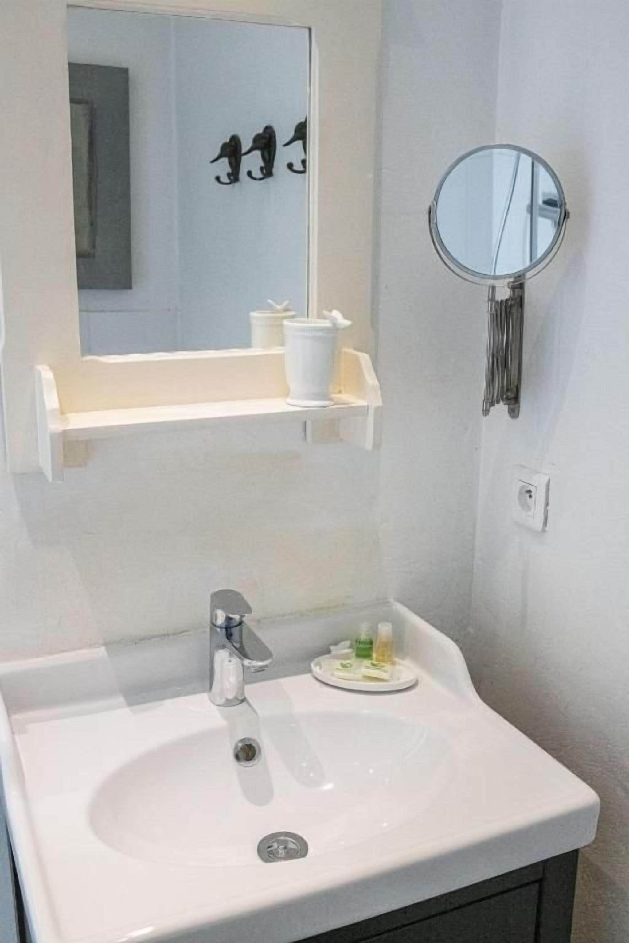 A bathroom with a white sink, a mirror, and a shelf with toiletries.
