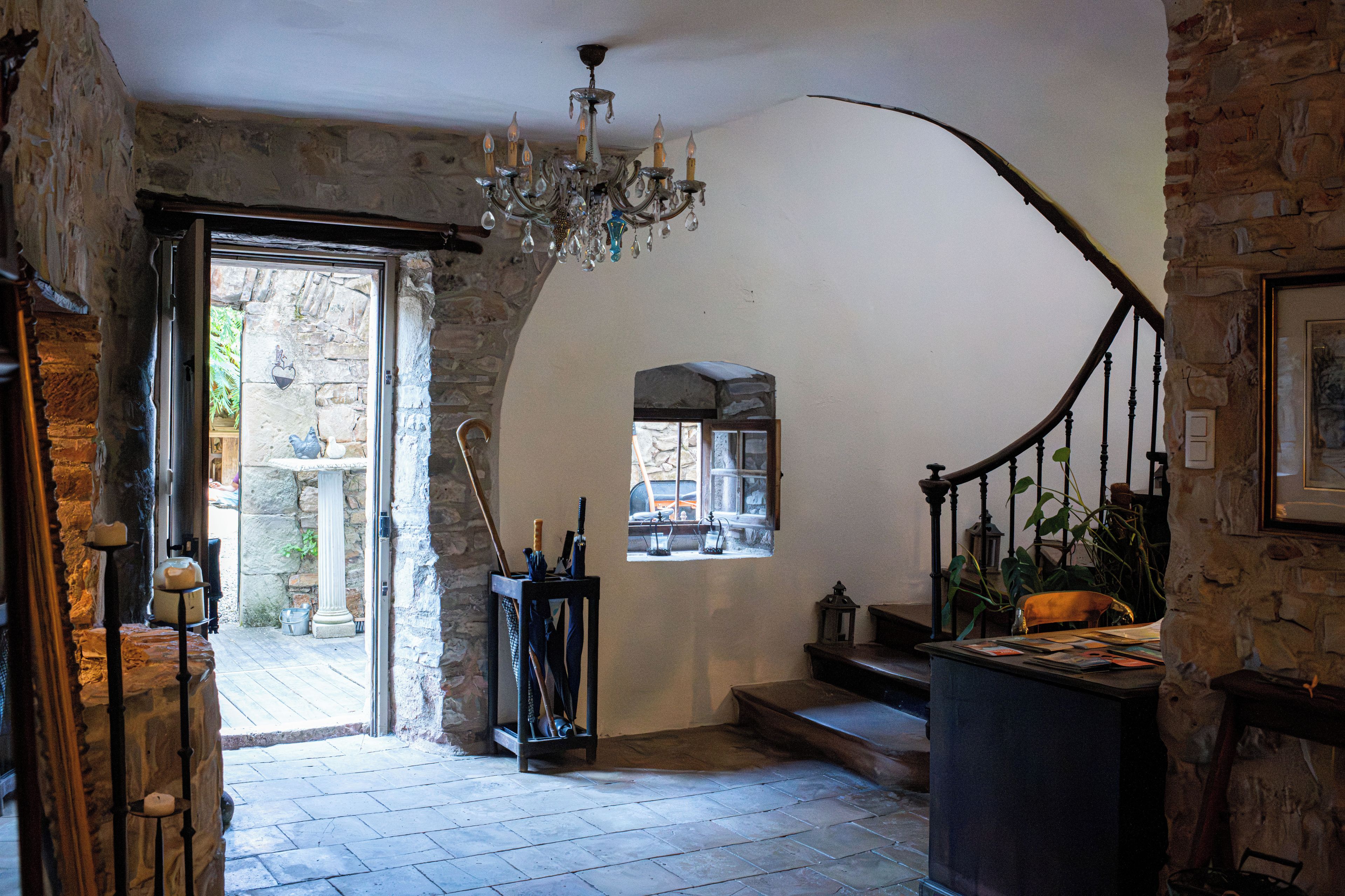 Quarto com parede de pedra, um candelabro, escada e janela com vista.