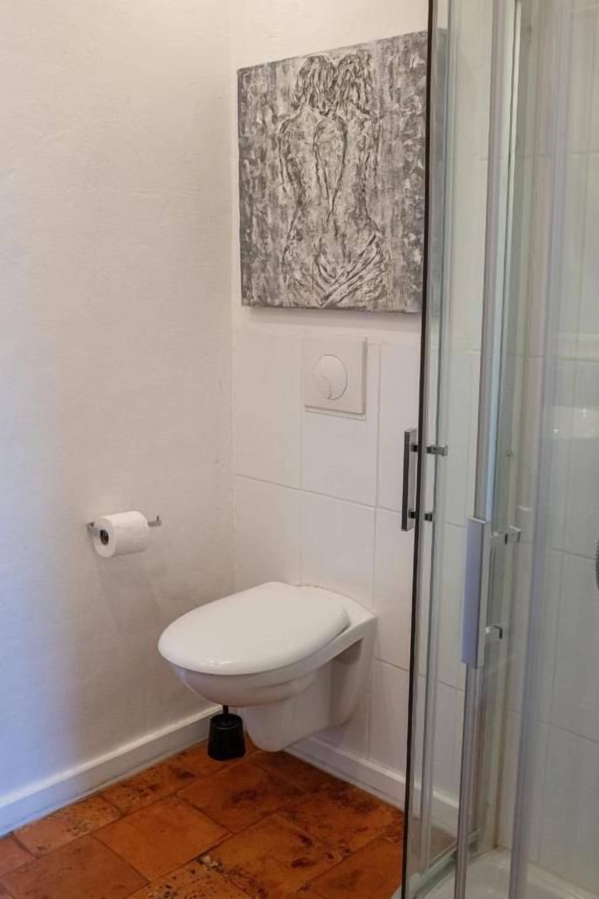 Un baño con inodoro, cabina de ducha de vidrio y una obra de arte colgada en la pared.
