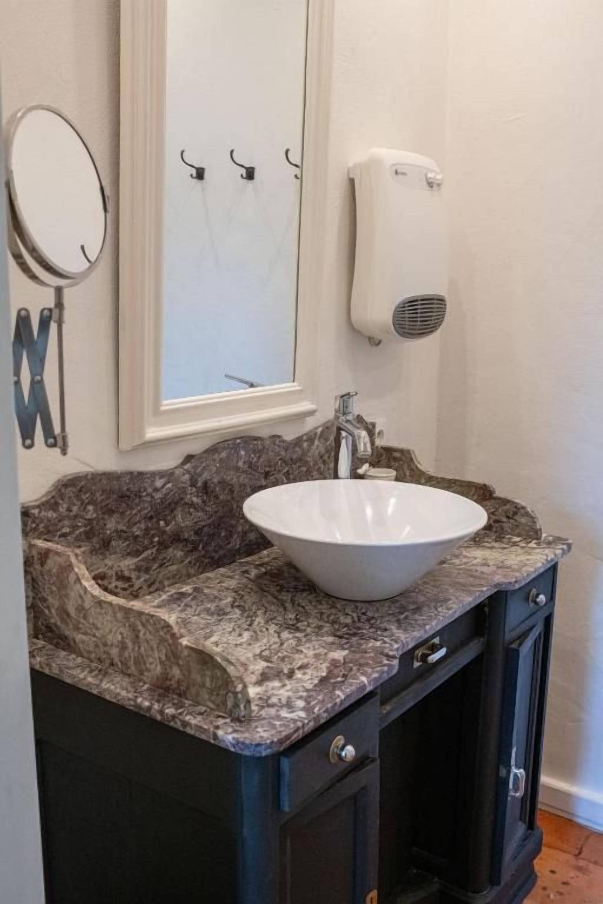 A bathroom with a granite countertop, a white sink, a mirror, and a towel dispenser.