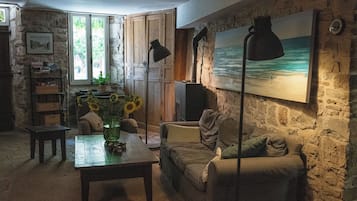 Una sala de estar acogedora con una pared de piedra, un cuadro de una playa, un sofá, una mesa de centro y una estantería.