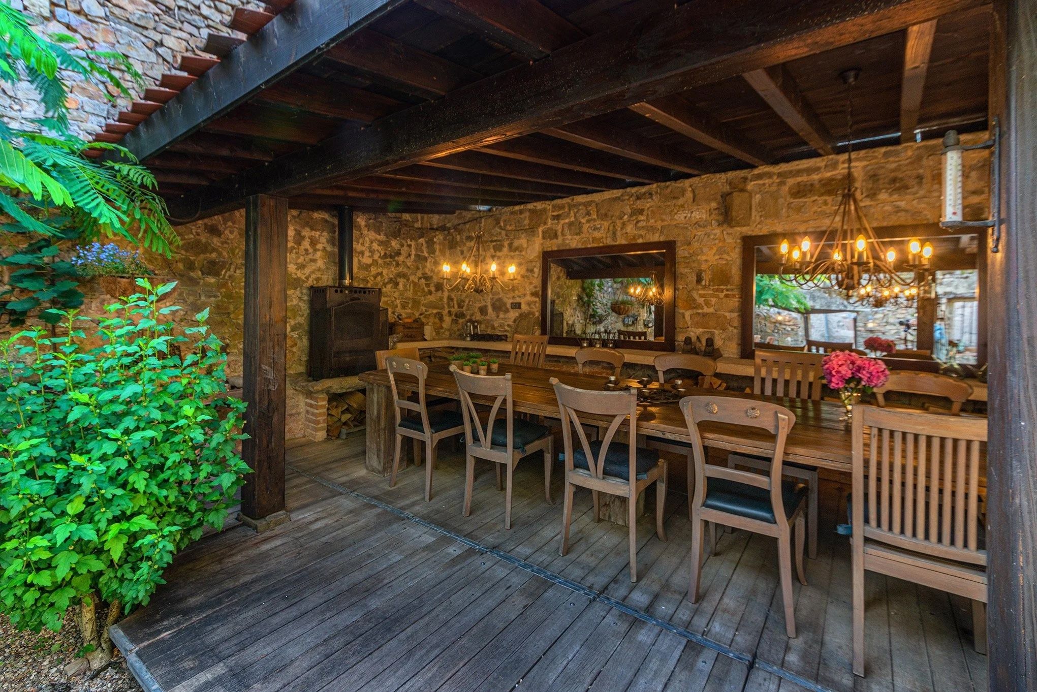 Un espacio de comedor al aire libre con paredes de piedra rústica, mesas y sillas de madera, y una chimenea de piedra.